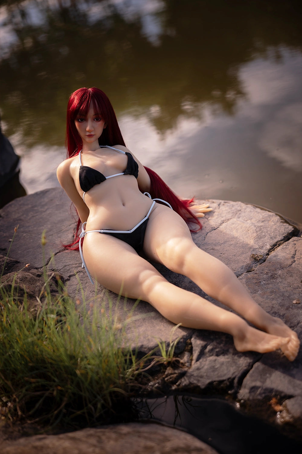 Image of A perfect reproduction of Puffypink, this small sex doll is posed on a rock by the water.